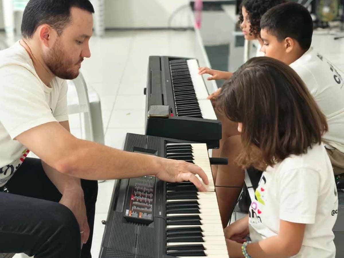 Professor ensinando teclado a três crianças durante uma aula do Nosso Cantinho